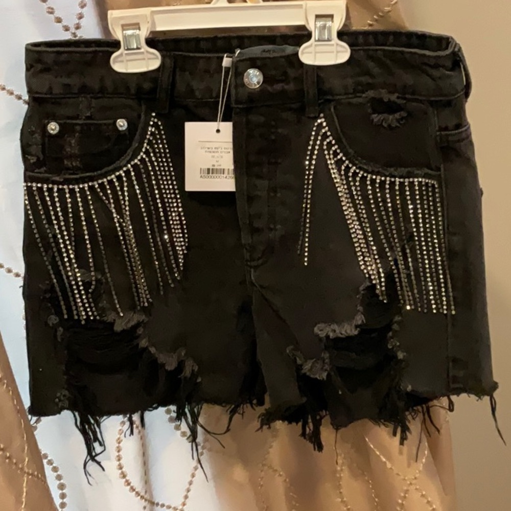 Black denim cutoff shorts with rhinestone fringe at pockets.